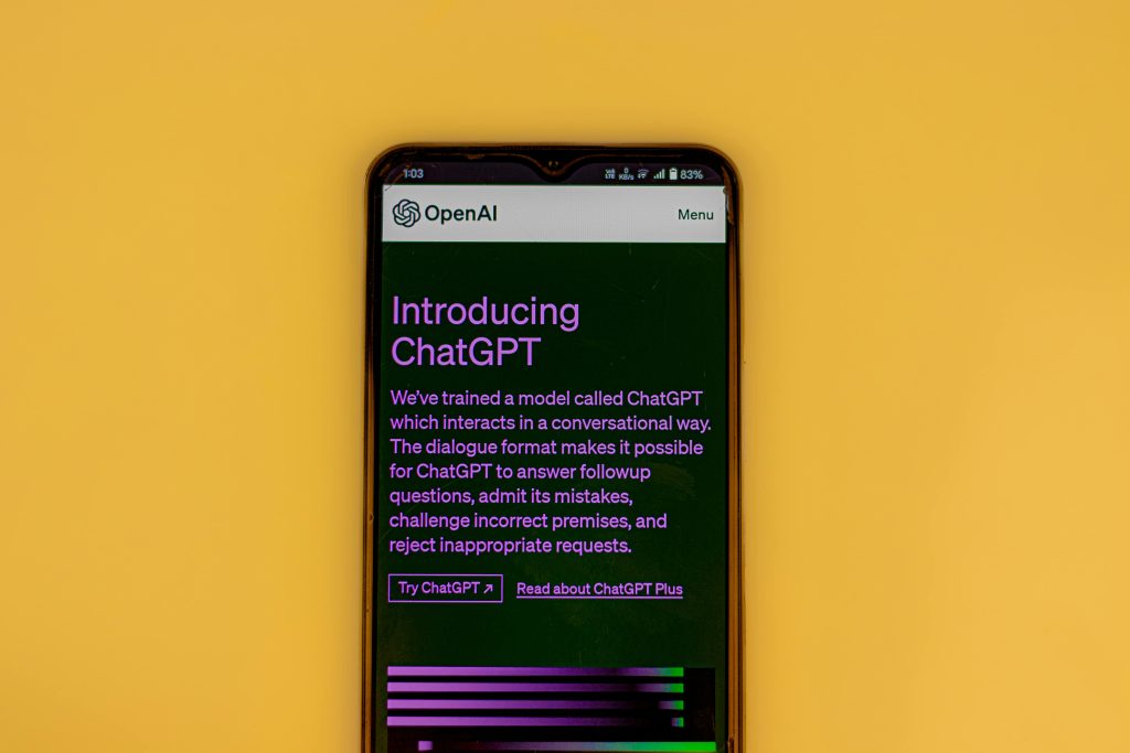 Mobile phone displaying the ChatGPT introduction screen with OpenAI branding on a yellow background.